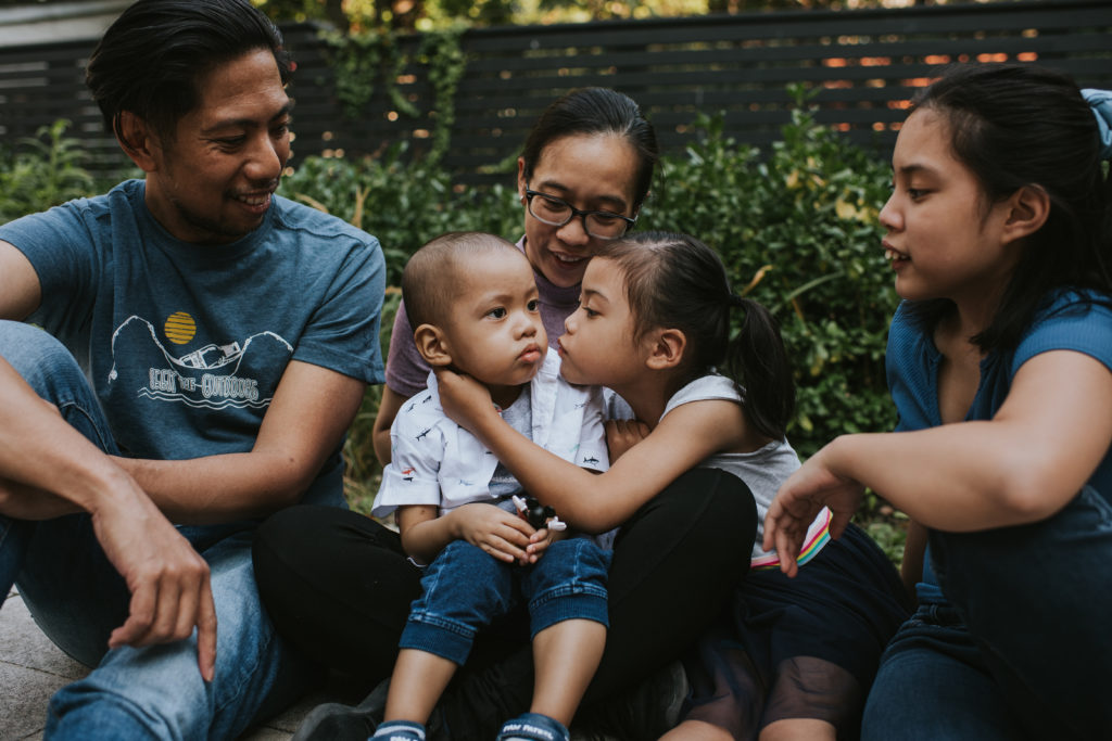 Dad, Mom, baby boy, young girl, and teenager girl sitting together.